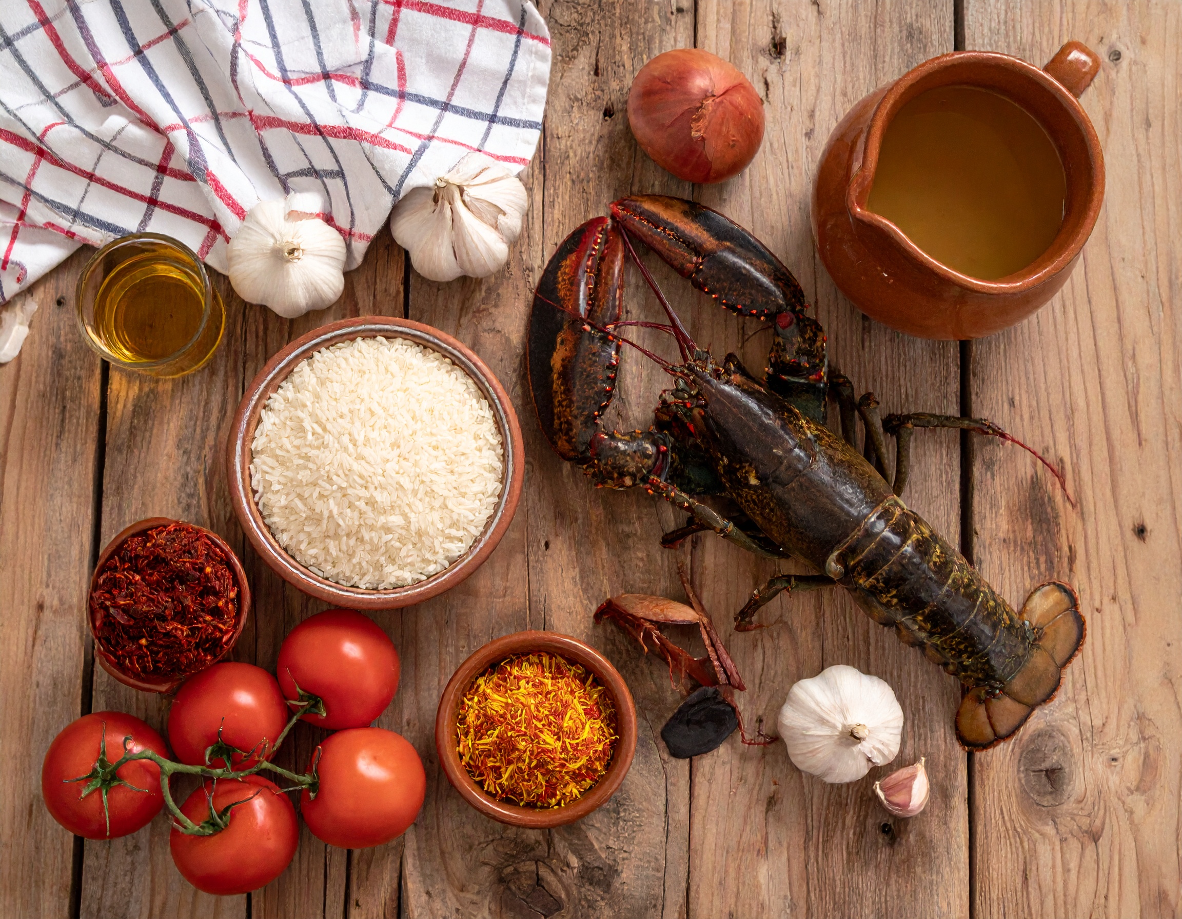 Bogavante vivo, arroz bomba, azafran y tomates sobre madera rustica
