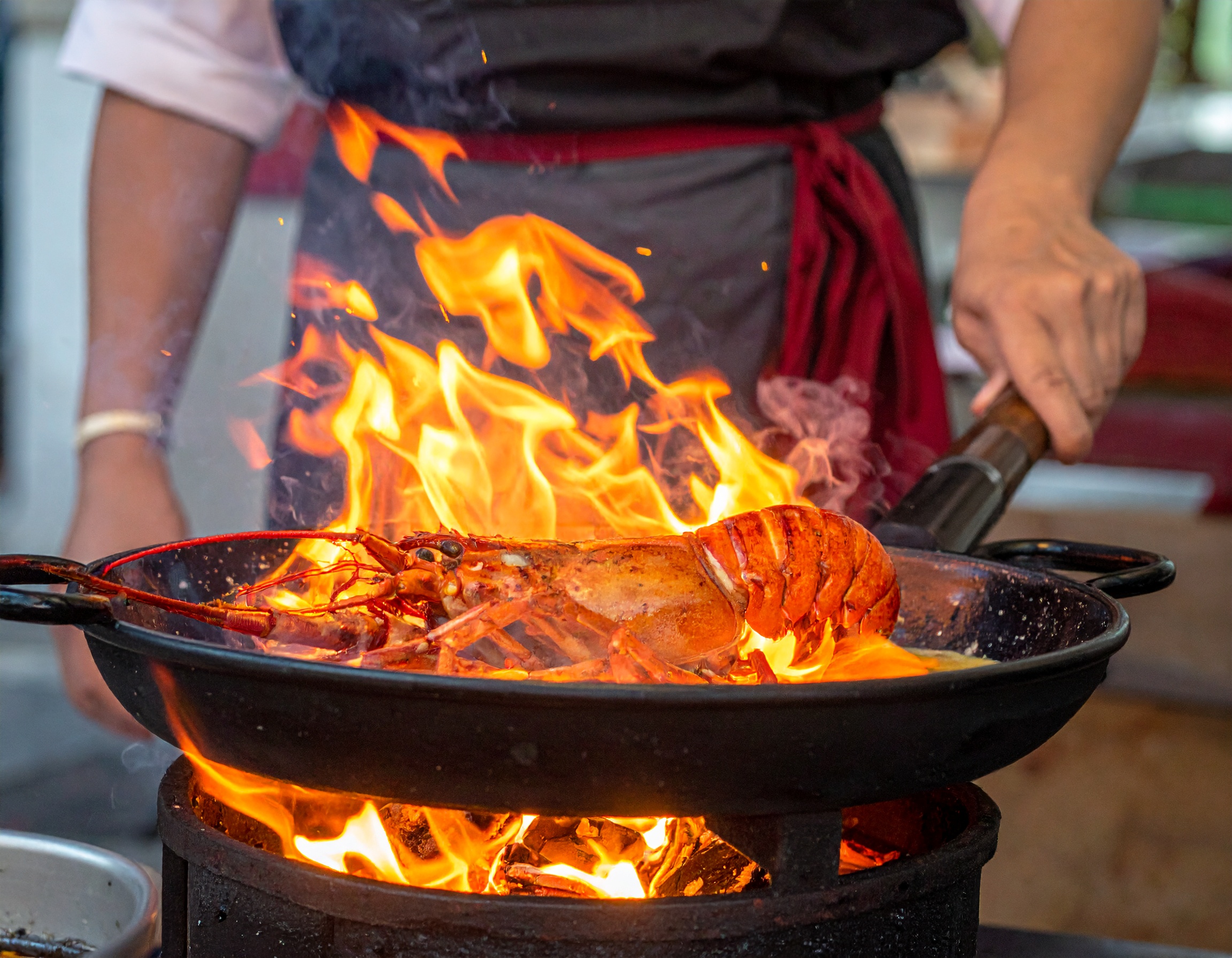 Bogavante flambeado con coñac en paellera con llamas dramaticas