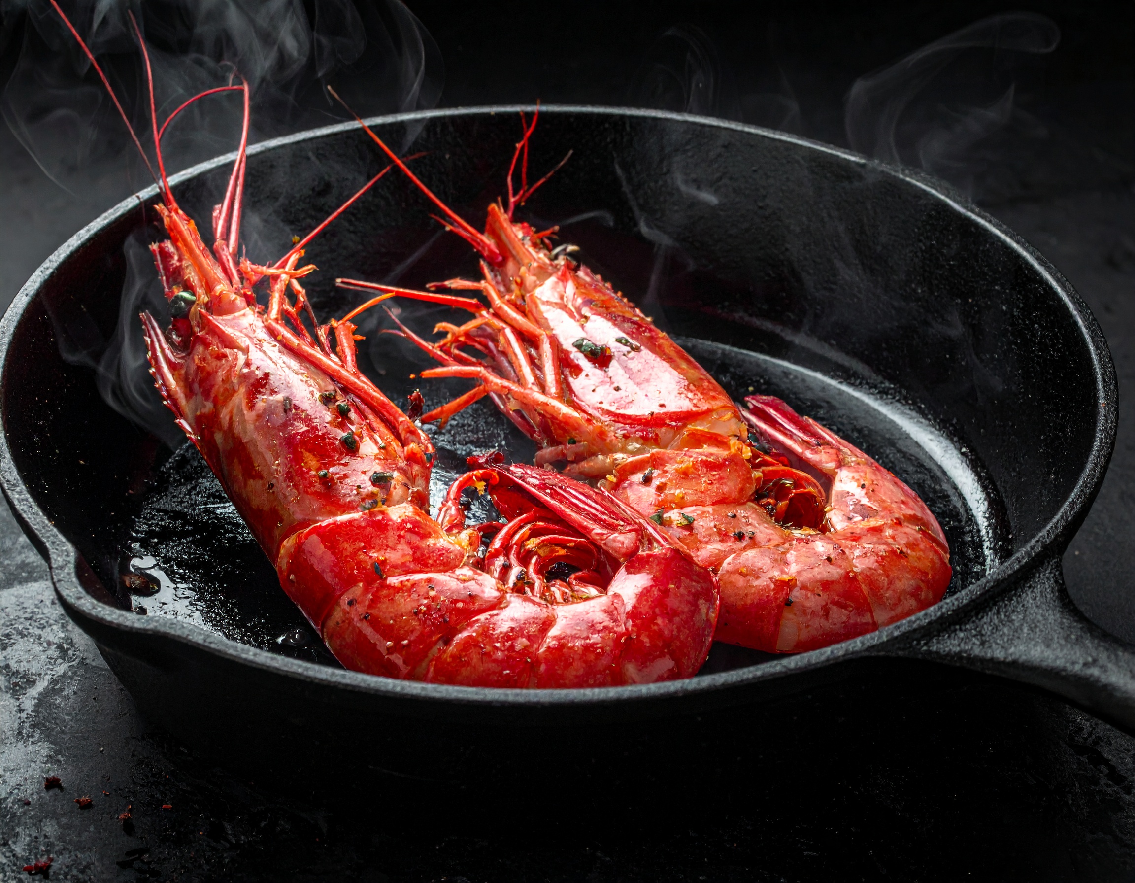 Dos gambas rojas de Palamós en sartén de hierro al rojo vivo, humo blanco subiendo