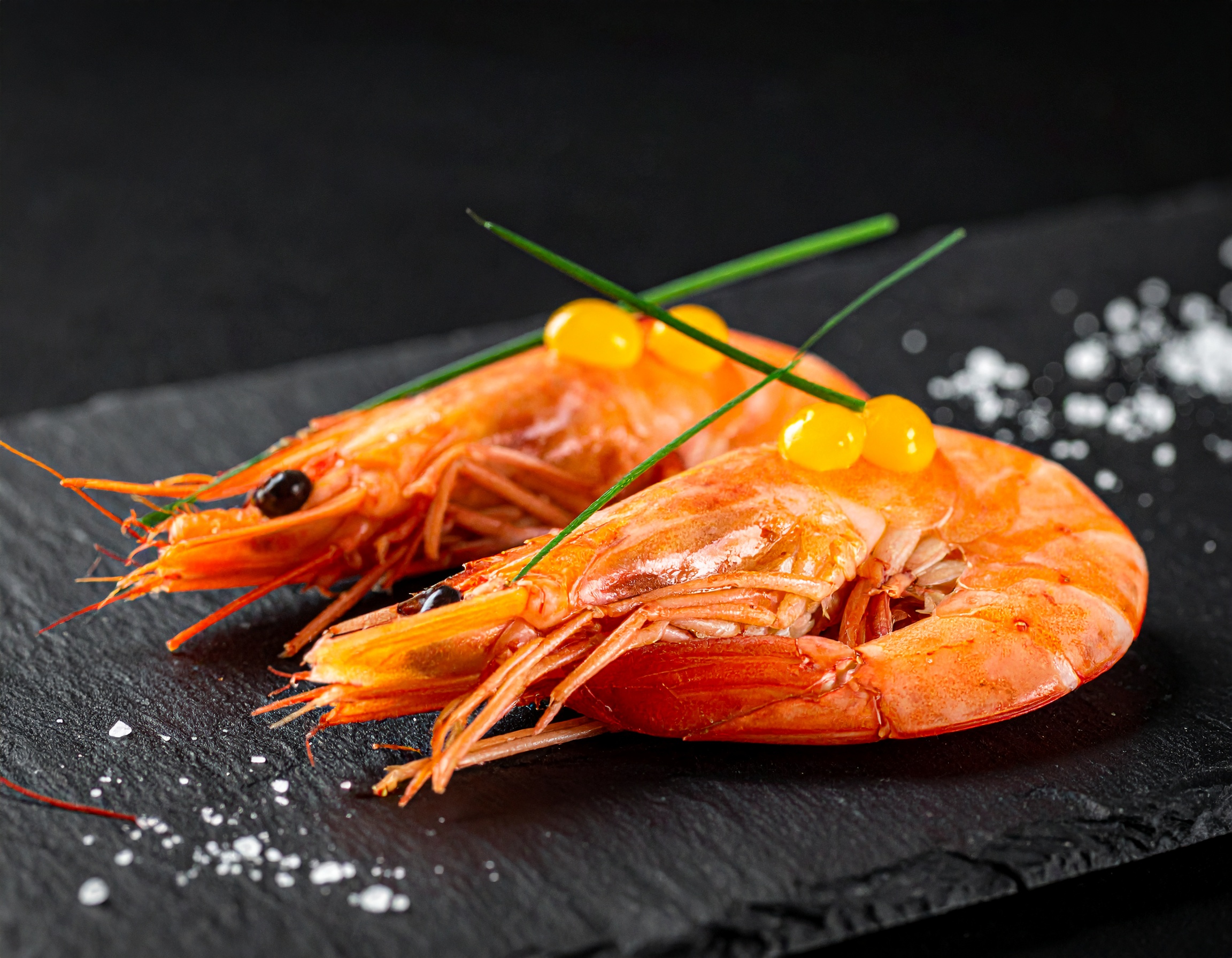 Dos gambas rojas de Palamós enteras sobre pizarra negra con esferas de yuzu amarillo, cebollino en diagonal y sal Maldon