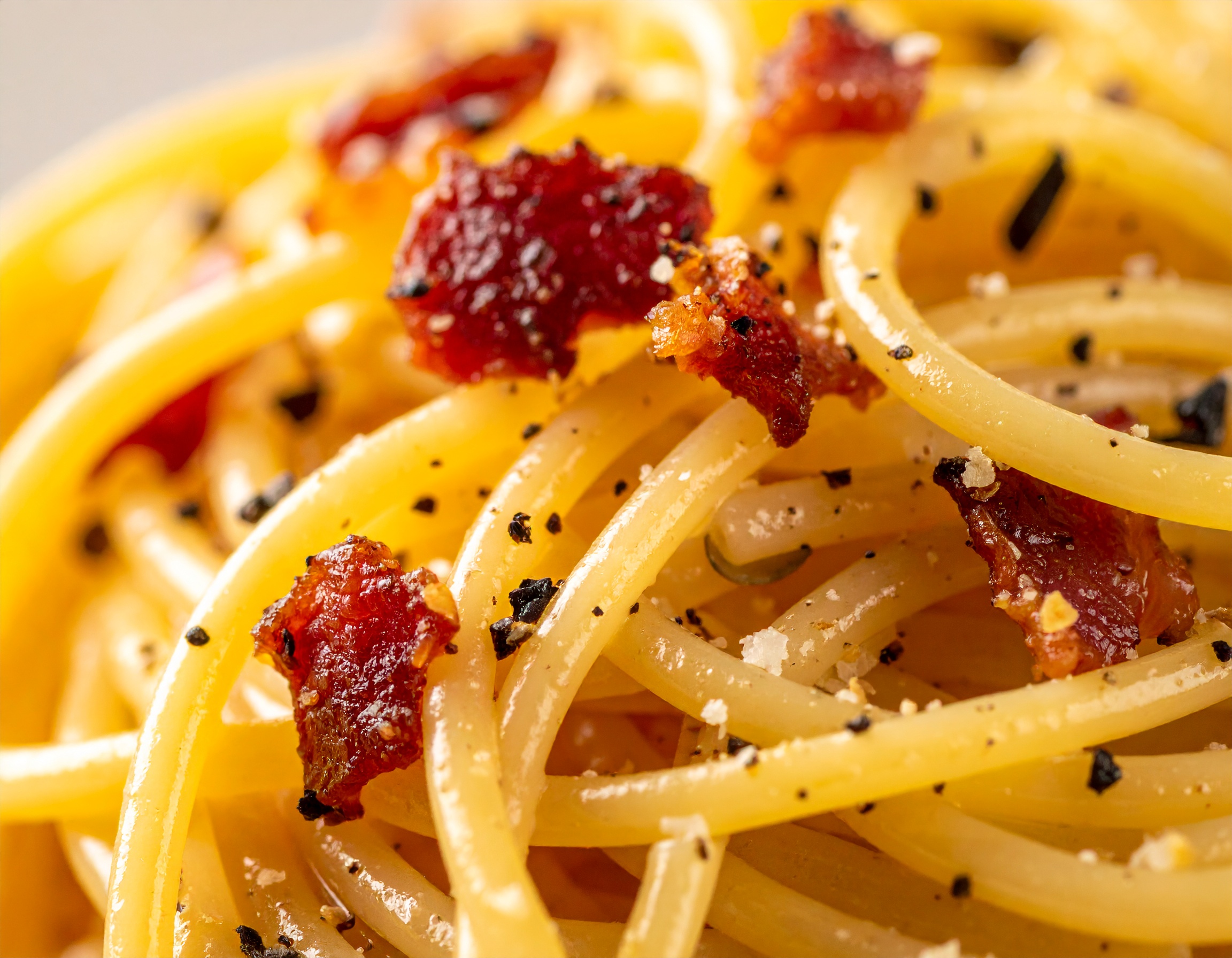 Macro de spaghetti carbonara brillantes con la emulsión dorada, trozos de guanciale crujiente y pimienta negra gruesa en primer plano