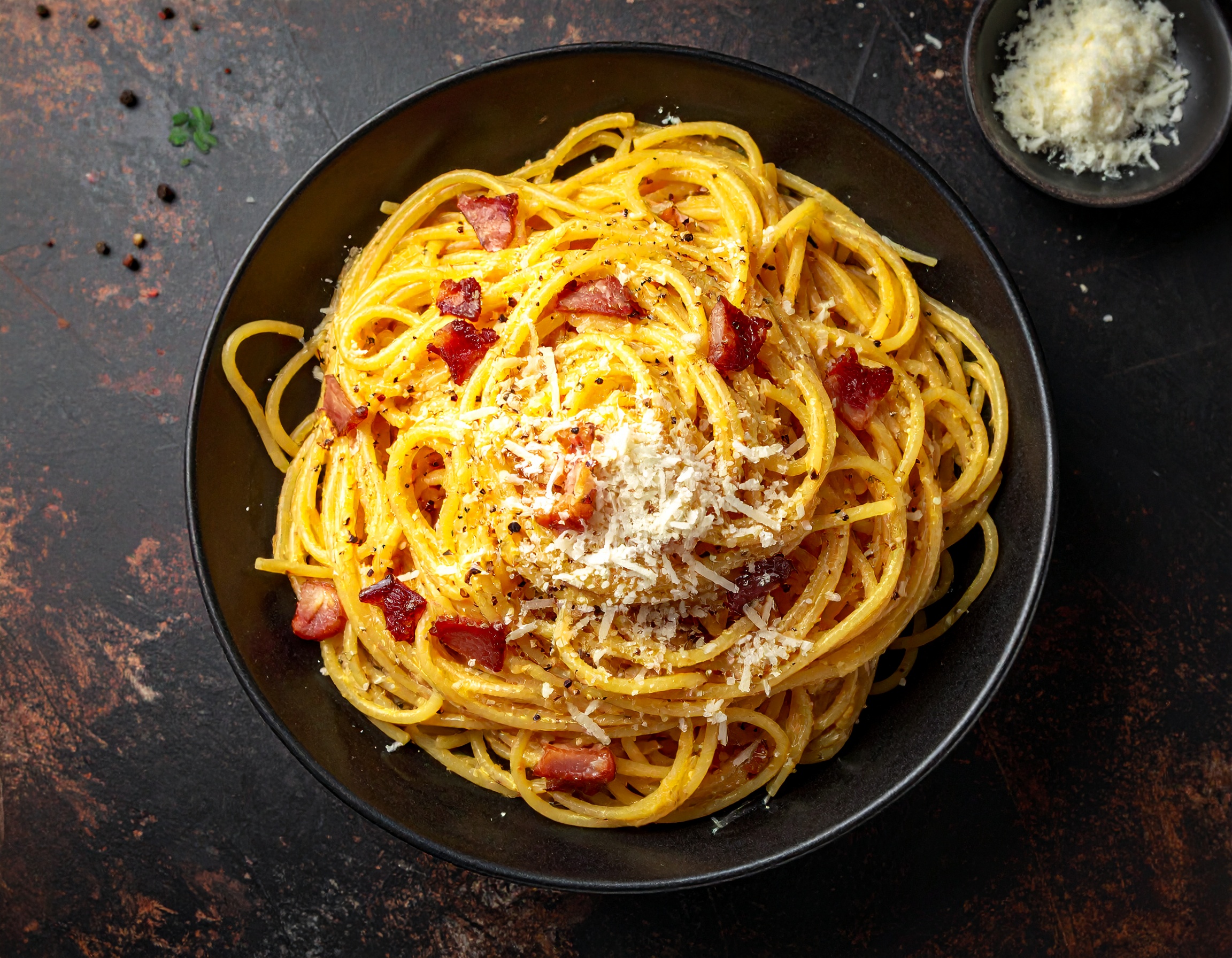 Creamy carbonara pasta in dark bowl, guanciale on top, rustic dark background