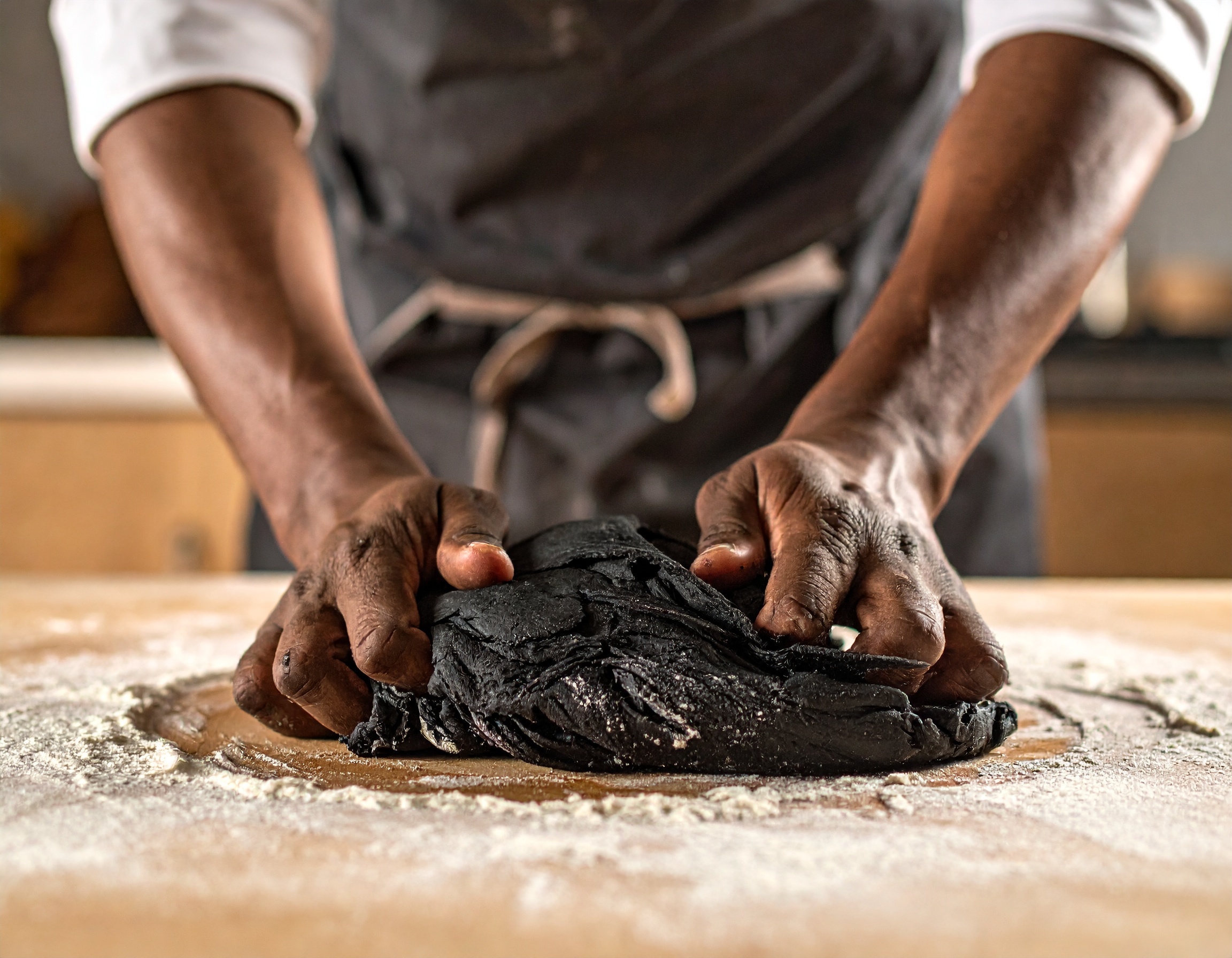 Manos del chef amasando la masa negra de tinta de sepia sobre superficie enharinada