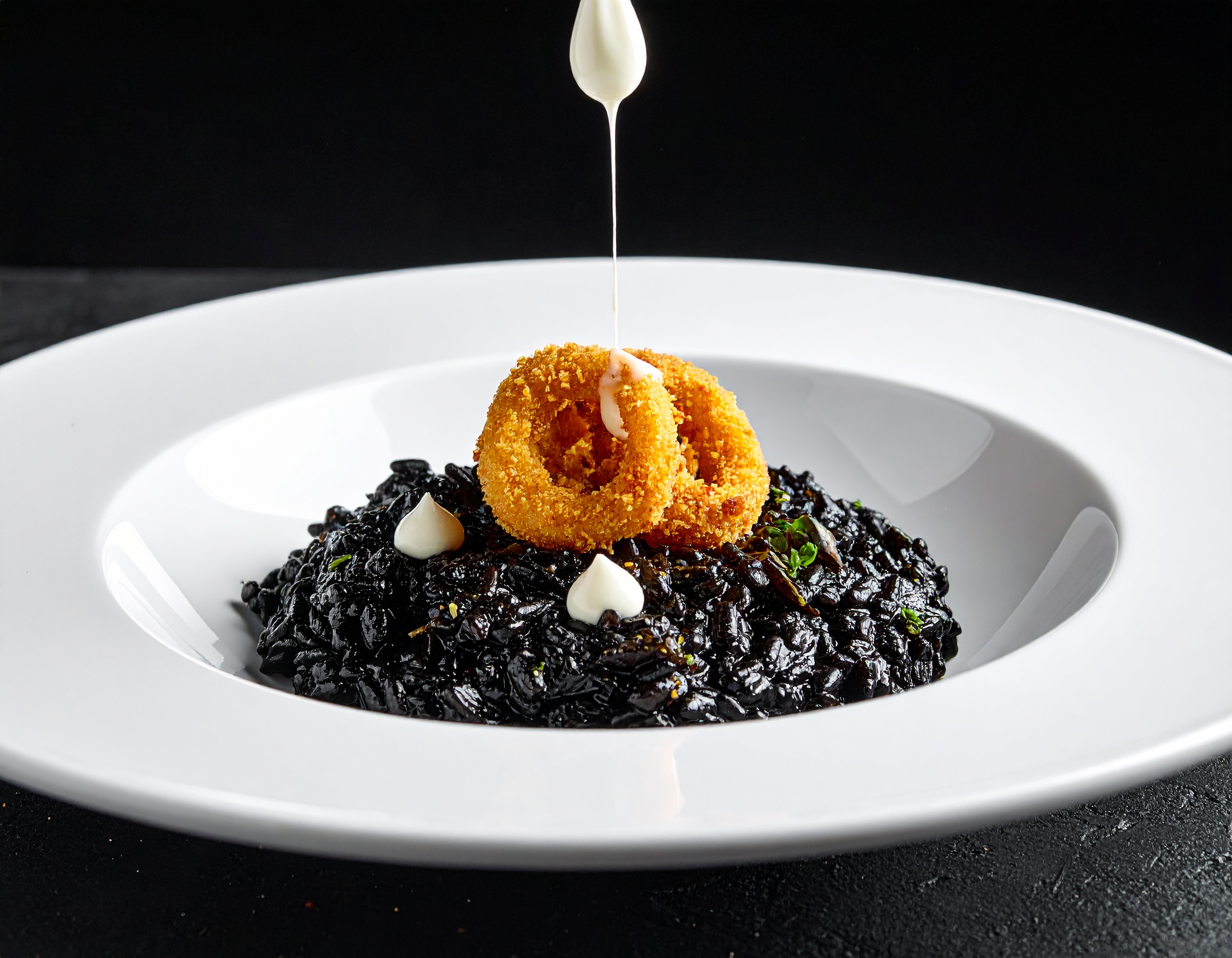 Risotto negro de sepia en plato blanco con dots de alioli de tinta y calamar crujiente dorado