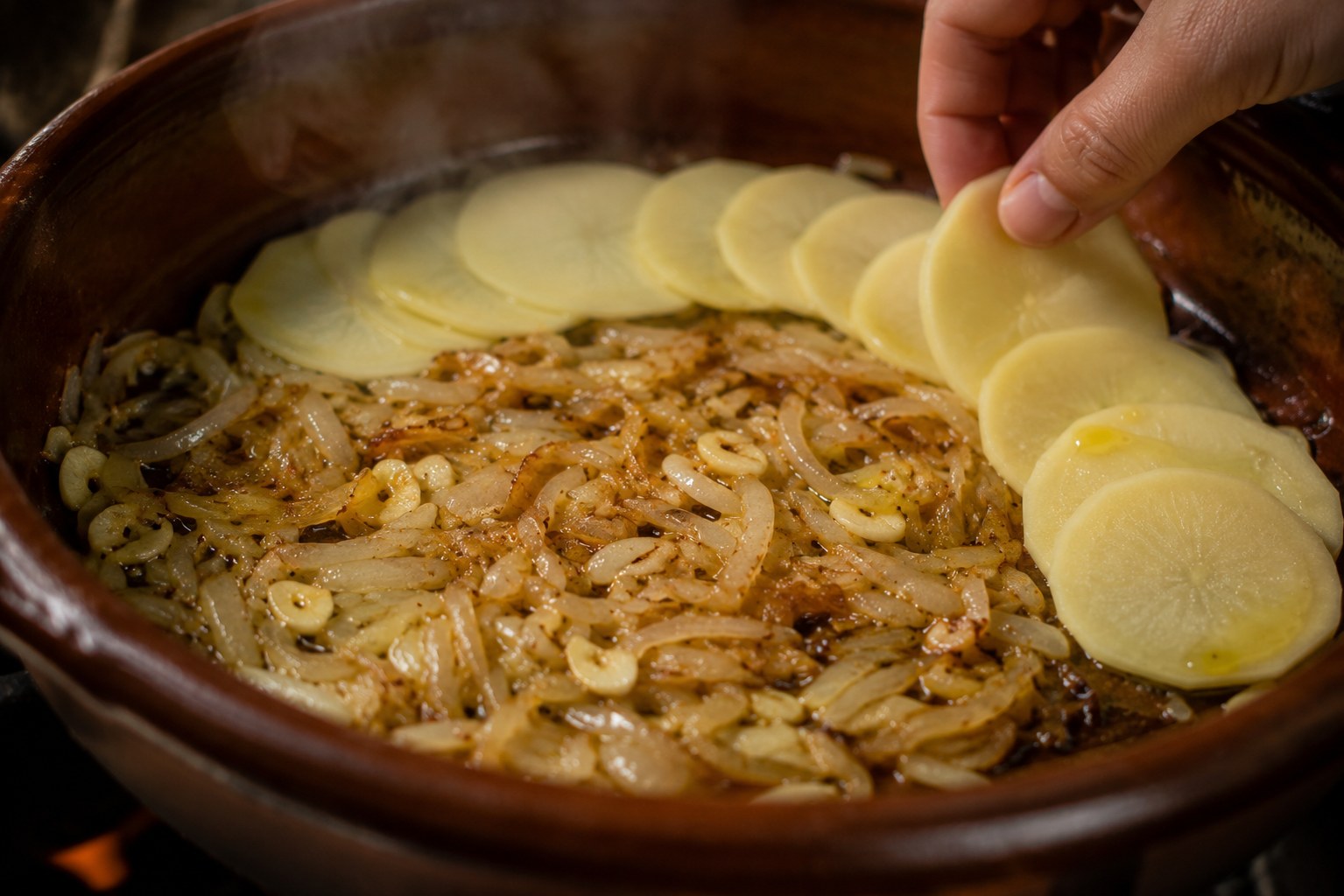 Sofrito de cebolla y ajo con láminas de patata en fuente de barro