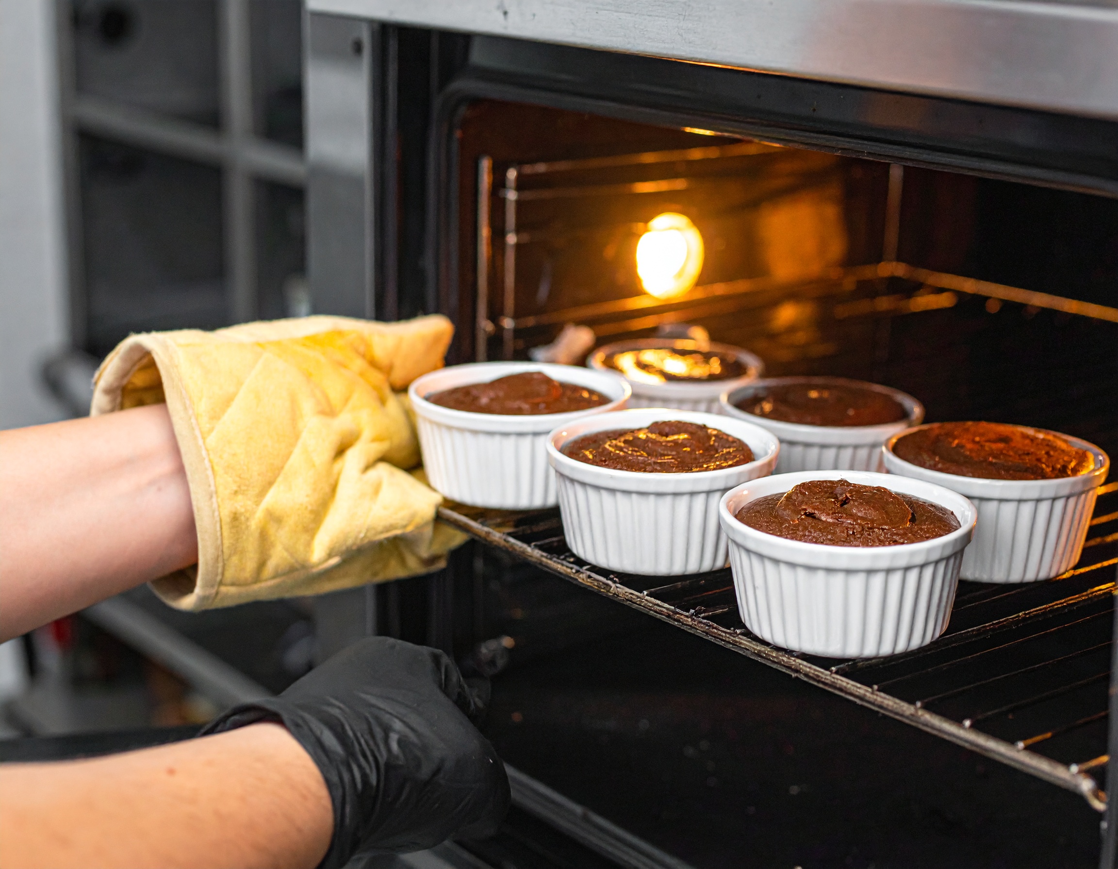 Soufflés de chocolate en ramequines blancos entrando al horno con manos enguantadas — luz interior del horno