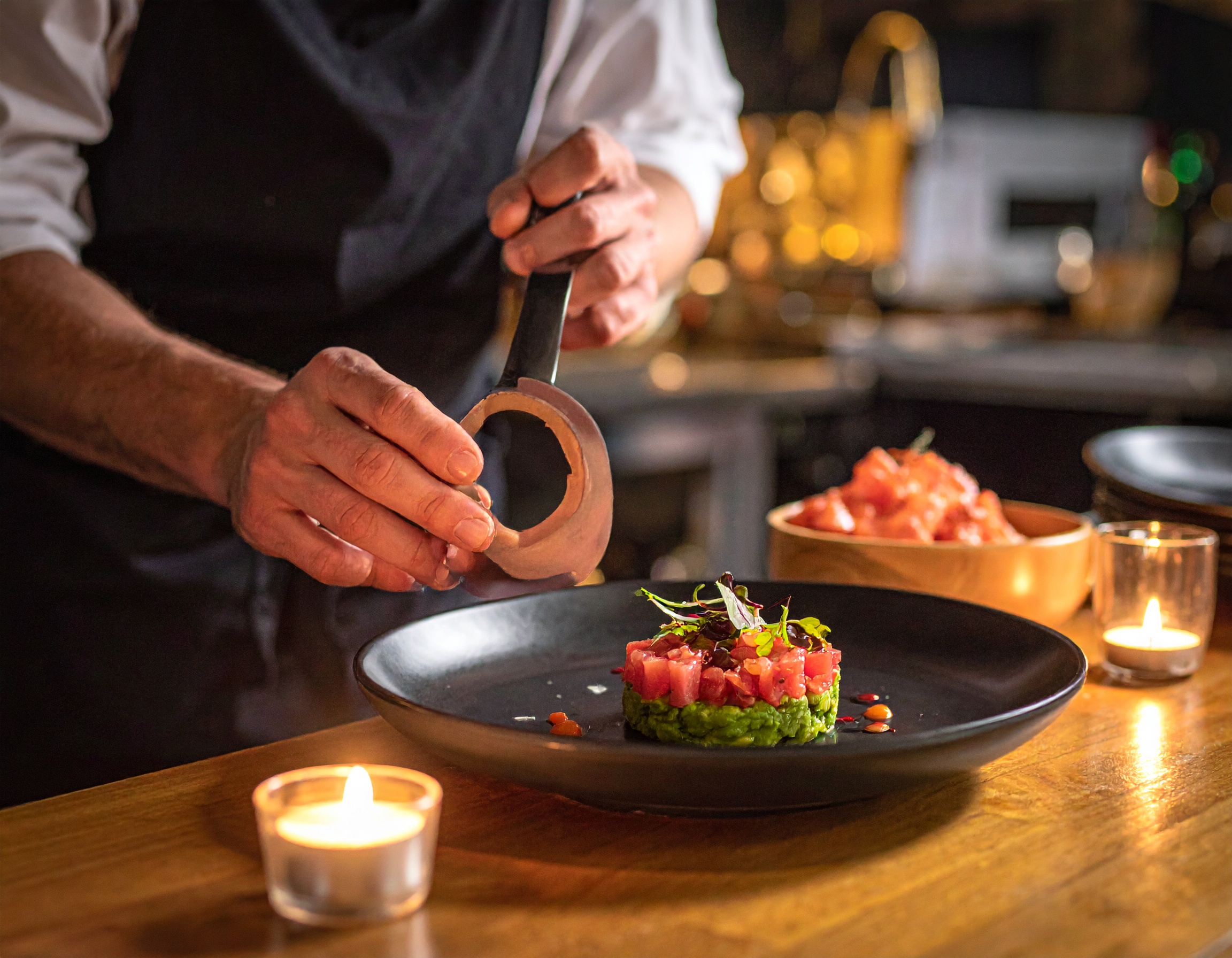 Chef retirando el aro de emplatado del tartar de atún Nikkei en restaurante con velas